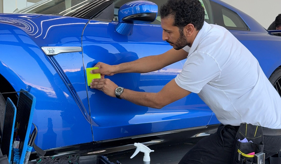 GenusCars expert applying PPF on blue sports car with squeegee and high precision